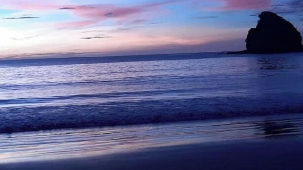 Una playa con la silueta de una formación rocosa y agua tranquila.