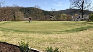 A golf course with a well-maintained green, a wooden fence, and a person in a red shirt. - Ozark Retreat~Walk-In~Pointe Royale Resort~Pools/Hottub (Branson)