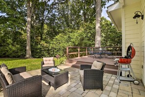 Relax on the patio with comfortable wicker sofas and a coffee table, surrounded by lush greenery and a barbecue grill.