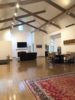 A spacious living room with a fireplace, a television, and a dining area with chairs and a table. - AMAZING HUGE GALLERY APARTMENT + FREE PARKING IN PRIME LOCATION (Wynnewood)
