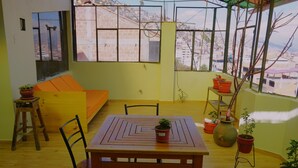 Una habitación con una mesa de madera, sillas, un sofá y plantas en macetas.