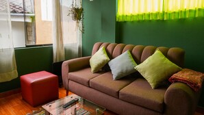 Una sala de estar acogedora con un sofá marrón, un reposapiés rojo y una mesa de centro de vidrio.