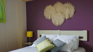 Una cama con ropa de cama blanca, cabecera y almohadas de varios colores.