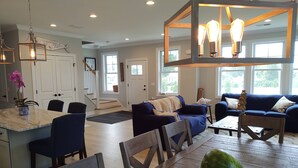 A spacious living room with a wooden dining table, blue sofas, and a large window providing natural light. - Summer Oasis in Narragansett! 5BR Home Perfect for Family & Friends! (Narragansett)