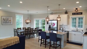 A modern kitchen with a central island, white cabinetry, and a 'Welcome' sign above the sink. - Summer Oasis in Narragansett! 5BR Home Perfect for Family & Friends! (Narragansett)