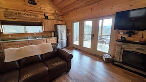 A wooden cabin interior with a leather couch, kitchen, sliding glass doors, and a fireplace. - Romantic Getaway! Hot Tub & Mountain Views, King Bed (whittier)