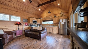 A cabin interior with a wooden ceiling, a sofa, a kitchen with wooden cabinets, a refrigerator, and a window. - Romantic Getaway! Hot Tub & Mountain Views, King Bed (whittier)