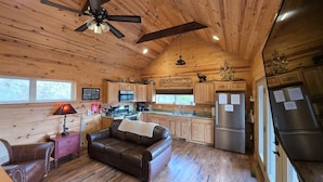 A cabin interior with a wooden ceiling, a ceiling fan, a kitchenette, a brown leather couch, and a dining table. - Romantic Getaway! Hot Tub & Mountain Views, King Bed (whittier)