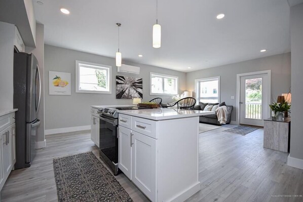 A spacious kitchen with a central island, a dining area with a sofa, and a view of the outdoors. - Promenade With All Inclusive Price, Close to Beach & Pier (Old Orchard Beach)