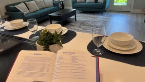 Un coin repas avec une table dressée pour deux personnes, un livre ouvert sur la table et un canapé vert en arrière-plan.