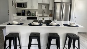Une cuisine moderne avec des meubles blancs, un réfrigérateur en acier inoxydable et un îlot central doté de tabourets de bar.