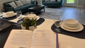 Un coin repas avec une table dressée pour deux personnes, un livre ouvert sur la table et un canapé vert en arrière-plan.