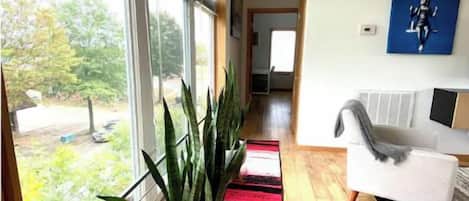 Un intérieur moderne avec une grande fenêtre, une plante en pot, un canapé blanc et un tapis coloré.