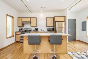 A modern kitchen with wooden cabinets, a central island with bar stools, stainless steel appliances, and a window providing natural light.