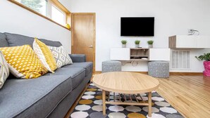 Een moderne woonkamer met een grijze bank, een ronde houten salontafel en een flatscreen televisie aan de muur.