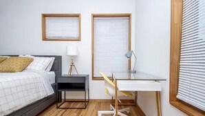 Een slaapkamer met een bed, nachtkastje, lamp en een bureau met stoel.