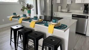 Una cocina moderna con armarios blancos, un refrigerador de acero inoxidable y una isla central con taburetes de bar.