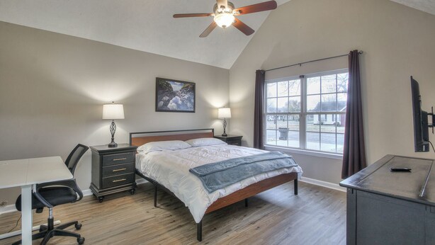 A bedroom with a bed, desk, chair, and a ceiling fan.