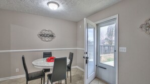 A dining area with a round table, four chairs, a 'WELCOME' sign, and a door leading outside.
