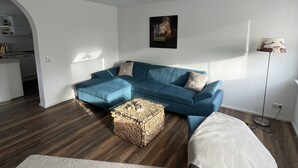 A modern living room with a blue sectional sofa, a glass coffee table, and a white rug.