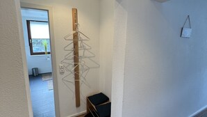 A hallway with a wooden floor, a hanging clothes rack, a small storage unit, and a window with a view of the outside.