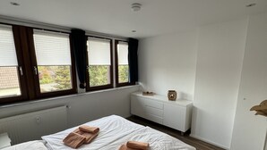 A modern bedroom with two beds, a white dresser, and a window with blinds.