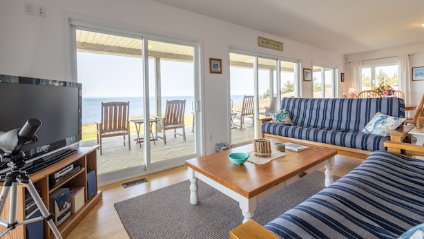 Een woonkamer met een grote televisie, houten meubels, een bank en uitzicht op de oceaan.