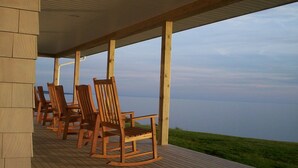 Een overdekt houten terras met schommelstoelen met uitzicht op een waterlichaam.
