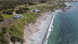 Luchtbeeld van een landgoed aan de kust, met een hoofdgebouw, kleinere gebouwen en een strand.