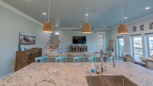 A spacious living area with a large kitchen island, pendant lights, and a television in the background.