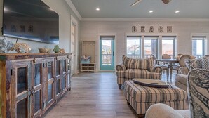 A spacious living room with a large TV, a ceiling fan, and a sign that reads "BEACH".