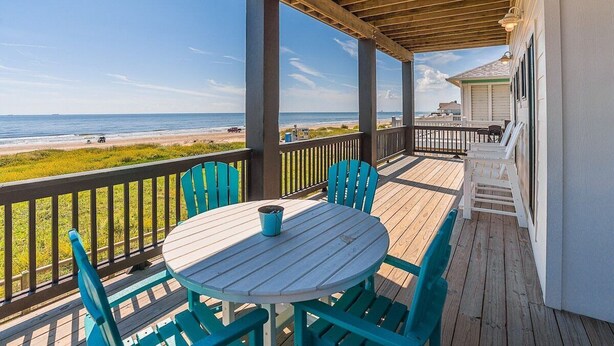 A covered outdoor seating area with a table and chairs, overlooking a beach.