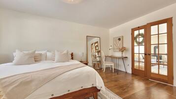 A bedroom with a large bed, a desk, and a view through a glass door.