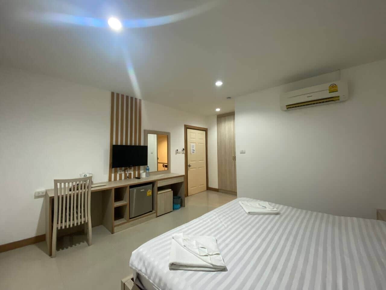A hotel room with a bed, a desk, a television, and an air conditioning unit.