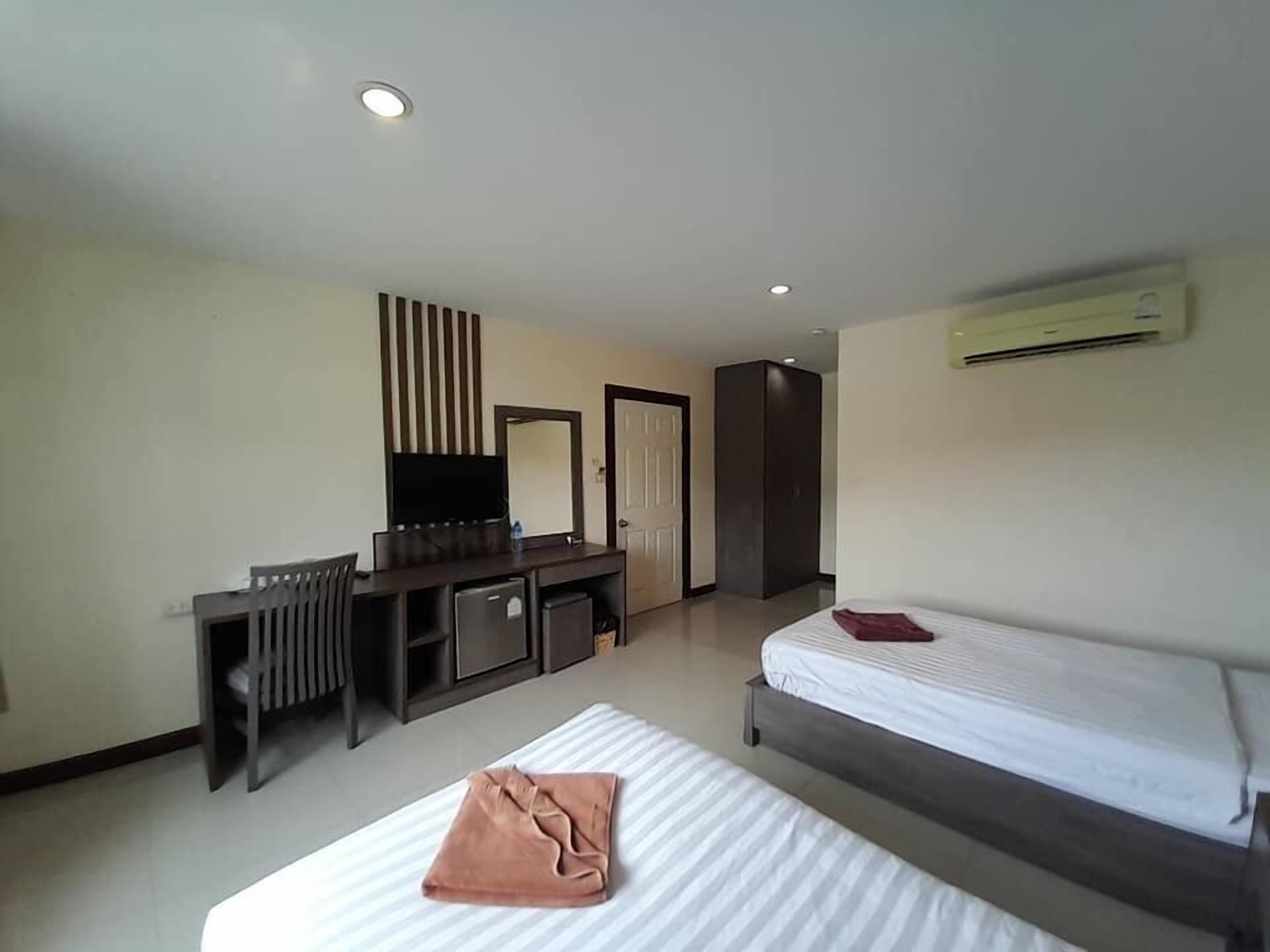 Quarto de hotel com cama, escrivaninha com televisão, espelho e guarda-roupa.