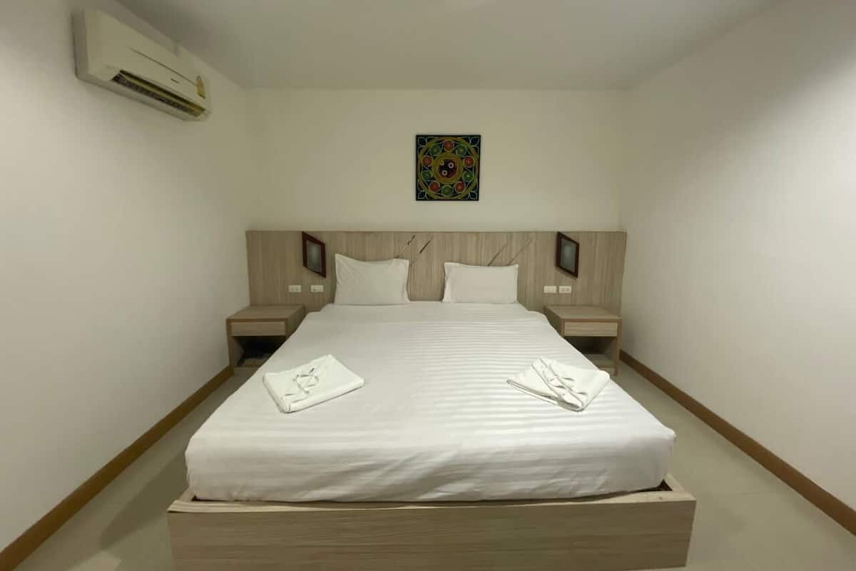 A hotel room with a large bed, wooden headboard, two bedside tables, and an air conditioning unit.