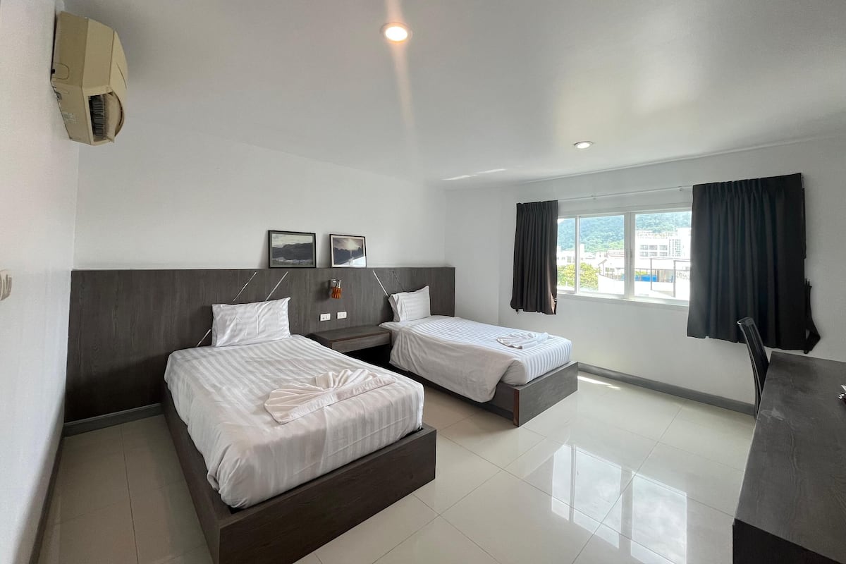A hotel room with two beds, a desk, and a window with curtains.
