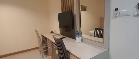 Habitación de hotel compacta con kitchenette, televisor de pantalla plana, espejo grande y pequeño escritorio.
