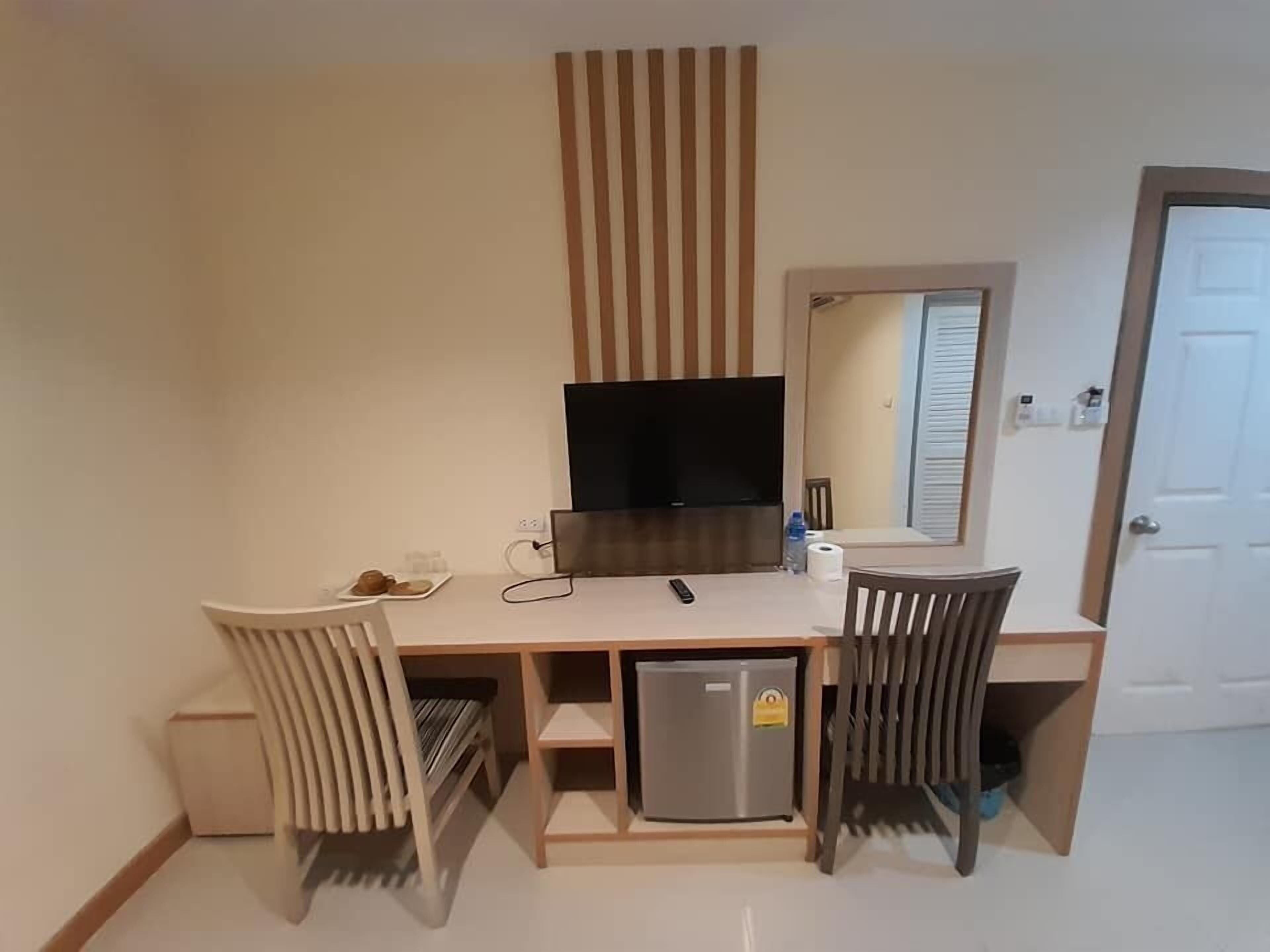 A compact hotel room with a kitchenette, a flat-screen TV, a small refrigerator, and a mirror.