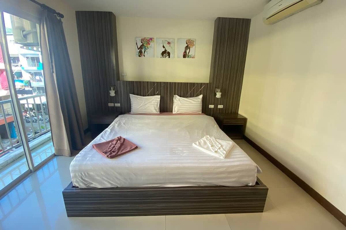 A hotel room with a large bed, a view of the outside, and a wall with three artworks.