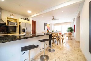 Una cocina moderna con encimera de mármol, electrodomésticos de acero inoxidable y una zona de comedor con mesa y sillas de madera.