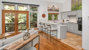 A modern kitchen with a large island, bar stools, and a view of the outdoors through large windows. - Beautiful Mountain Home With Hot Tub on Free Bus Route (Vail)