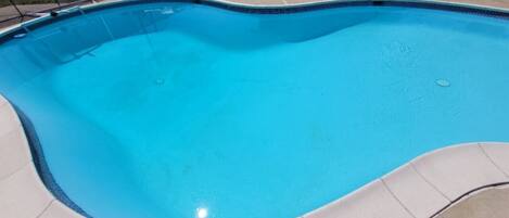 A swimming pool with a curved edge, surrounded by a tiled deck.