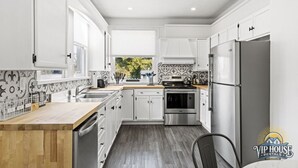 Une cuisine moderne avec des meubles blancs, un réfrigérateur en acier inoxydable et un plan de travail en bois.
