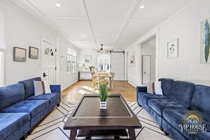 Een ruime woonkamer met twee blauwe banken, een centrale salontafel en een eethoek op de achtergrond.