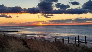 Une plage bordée d’une clôture en bois et de dunes herbeuses.