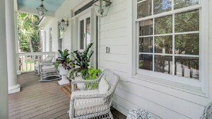 A covered porch with white wicker furniture, potted plants, and large windows. - Award-Winning Resort Amenities | Fairway Oaks 33 (Isle of Palms)