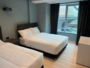 A hotel room with two beds, a large window with curtains, a bedside table, and a small cabinet. - Hotel HTL (Bogotá)
