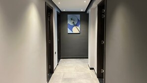 Un pasillo moderno con paredes oscuras, luces empotradas en el techo y suelo de baldosas.