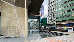 Una calle urbana moderna con un edificio que cuenta con amplios ventanales de vidrio y una estructura metálica en la parte superior.